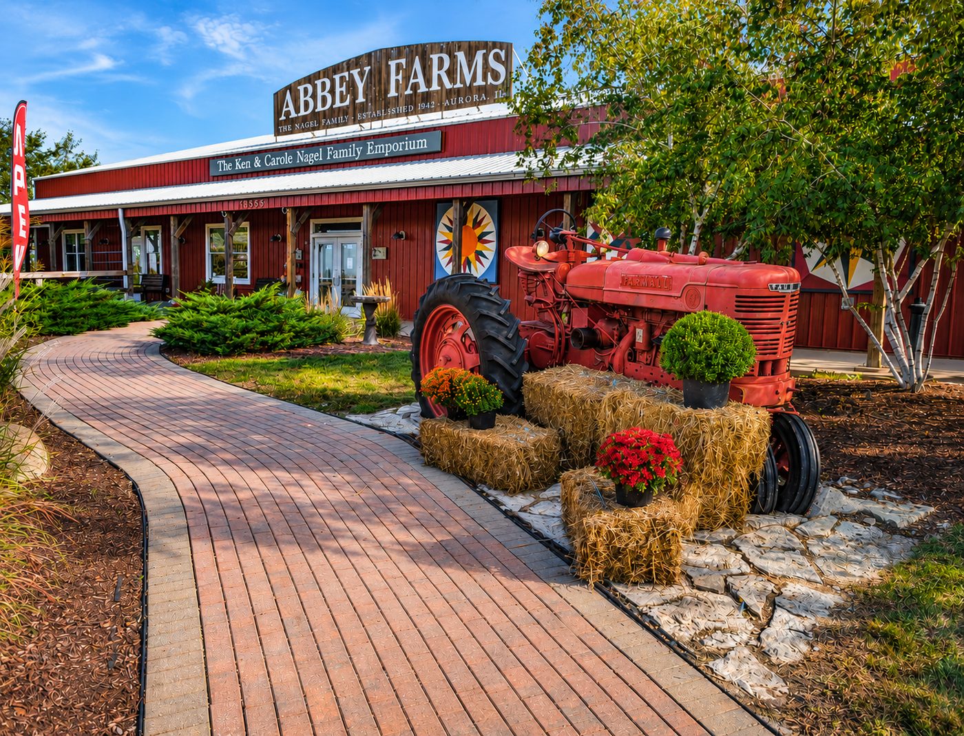 The red Abbey Farms Emporium building with the vintage Farmall tractor, hay bales, and brick path