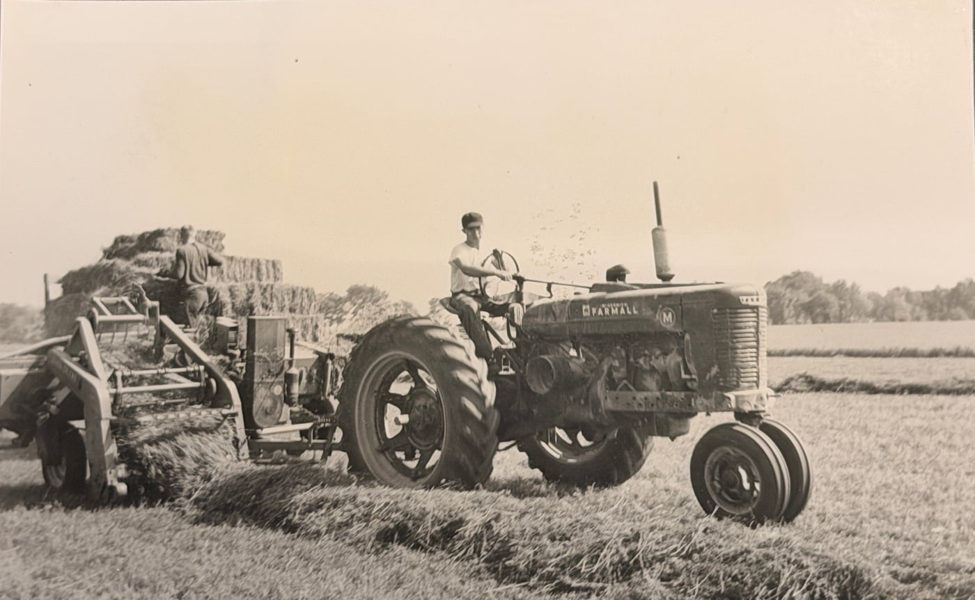 Two young Marmion monks baling hay with a Farmall tractor in a field, summer 1954